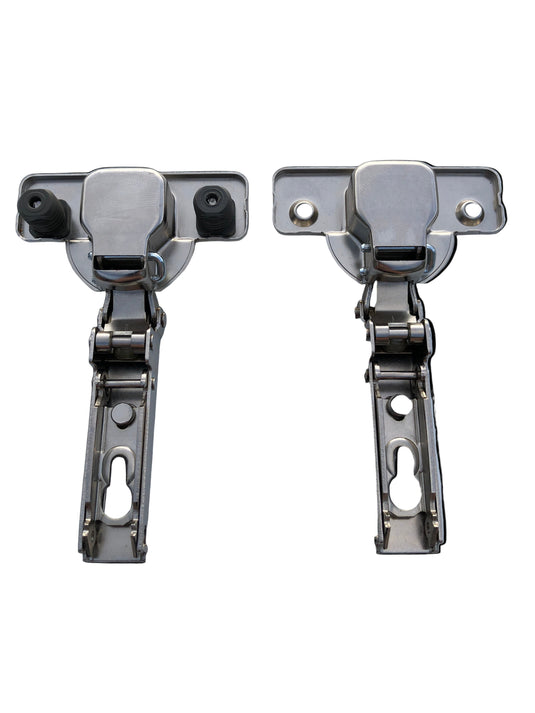 Two cabinet hinges with attached screws and dowels on a clear surface.